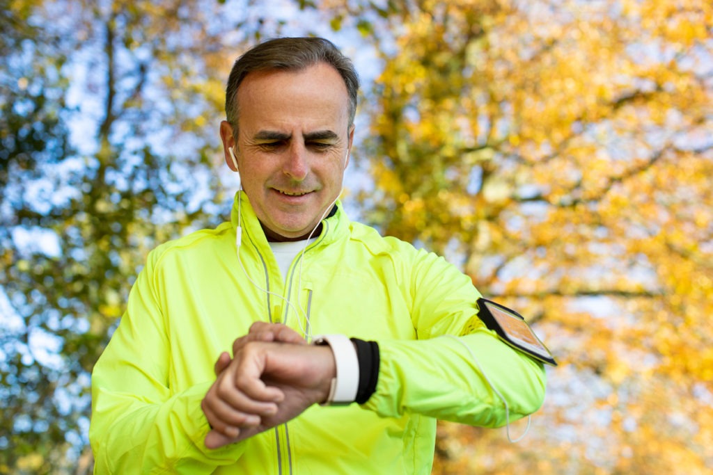 Mature Man Exercising In Autumn Woodland With Activity Tracker