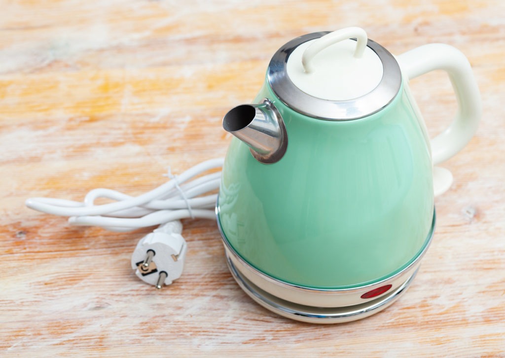Metal light green electric kettle on wooden surface