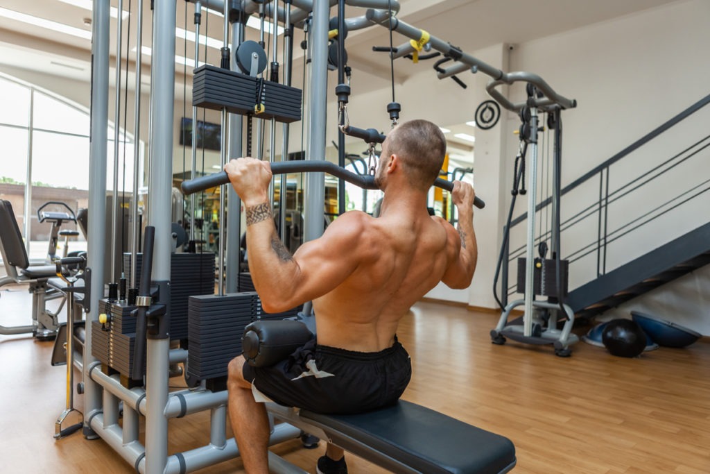 Fitness muscular man with naked torso working out in lat pulldown exercise machine in gym