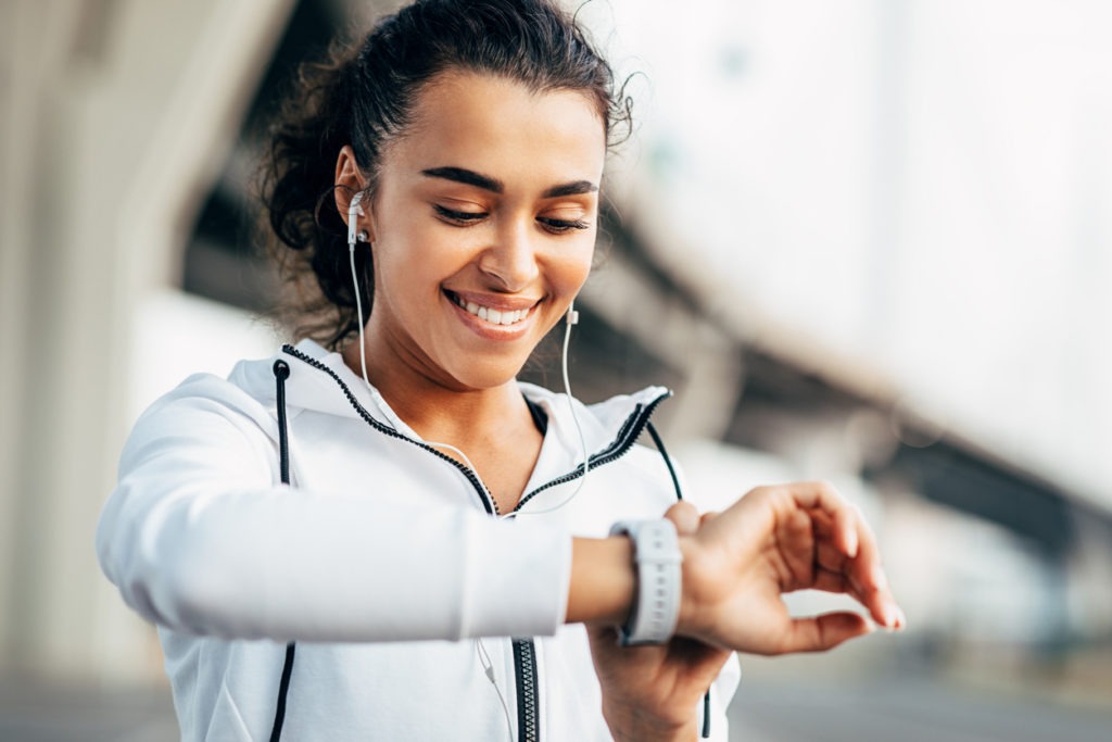 Smiling woman checking her physical activity on smartwatch. Young female athlete looking on activity tracker during training