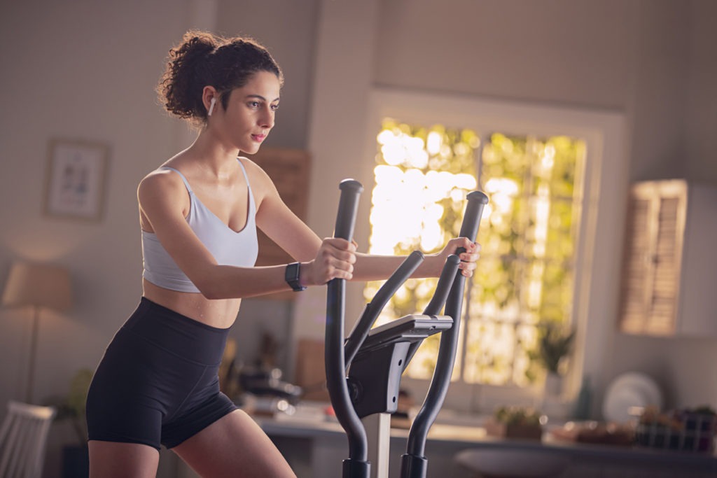 Young woman doing exercise on cross-trainer at home
