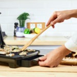 Woman holding spatula for cooking and serving barbecue on table. Grill steak on an electric stove at kitchen