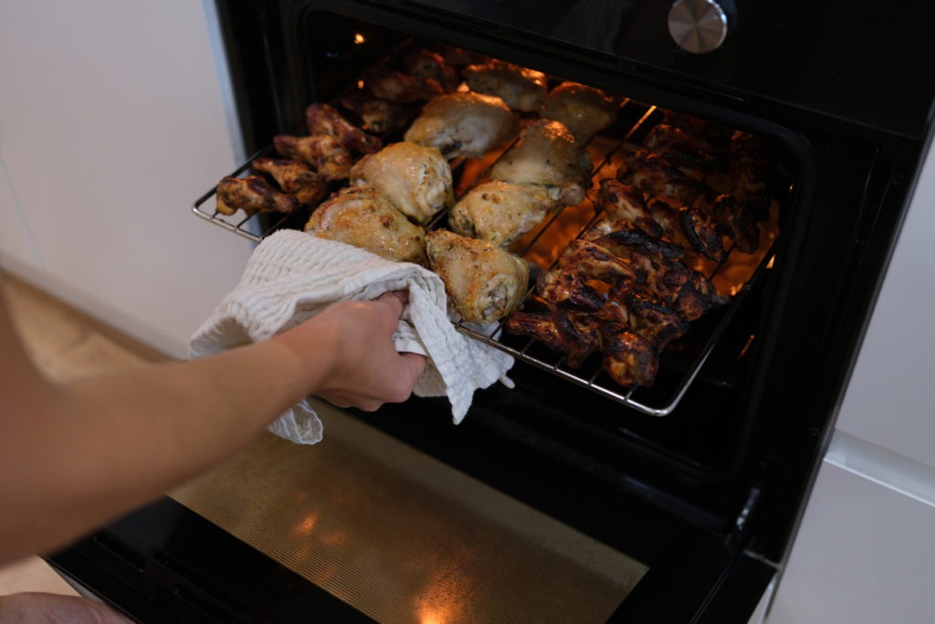 Woman taking out grill of baked chicken from oven closeup