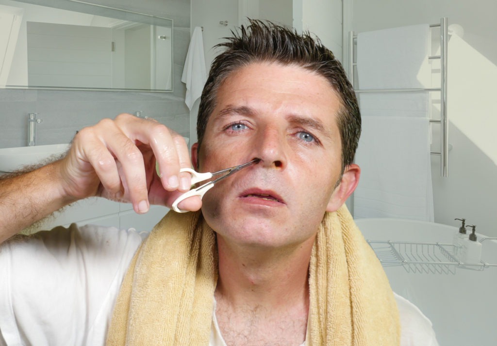 lifestyle natural portrait of young attractive and concentrated man cutting carefully hairs in his nose with small scissors at home bathroom in male beauty and domestic hygiene concept