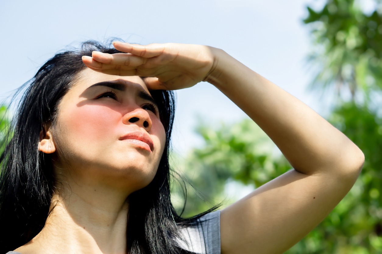 Asian woman having problem sunburn redness on face skin hand cover her face to protect ultraviolet from sunlight standing outdoors under sunny