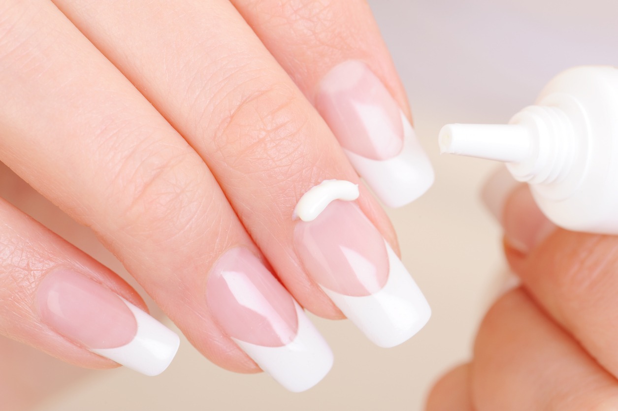 Woman caring of her finger applying the moisturizing cosmetic cream on fingernail