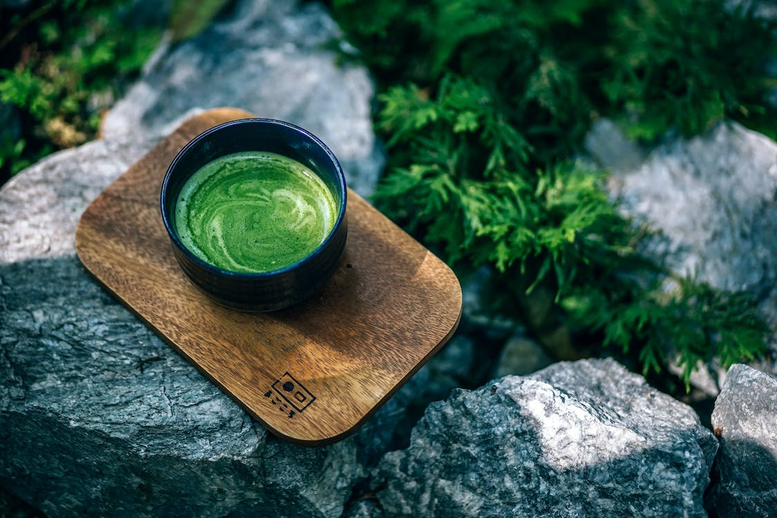 a cup of green tea on top of a wooden plank on a stone