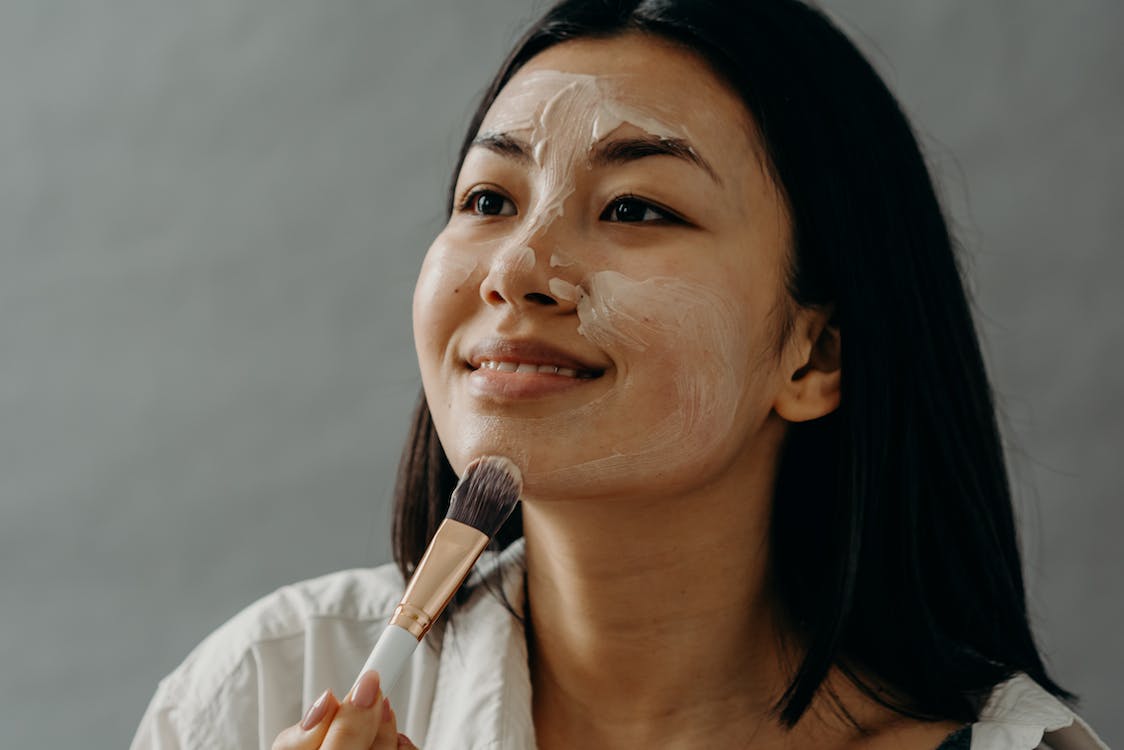 a woman applying cream on her face with a brush