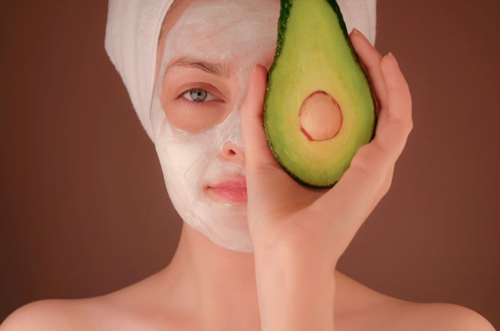 a woman in a white robe, covering half of her face with avocado
