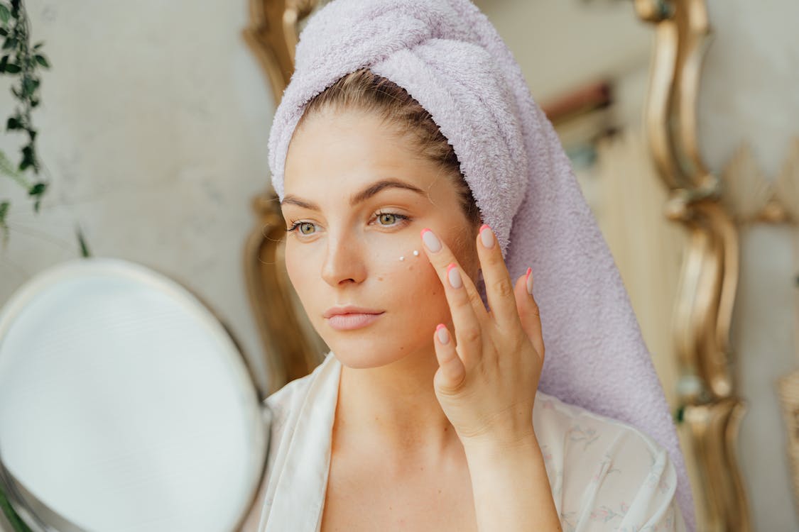 a woman with a towel on her head while applying cream on her face