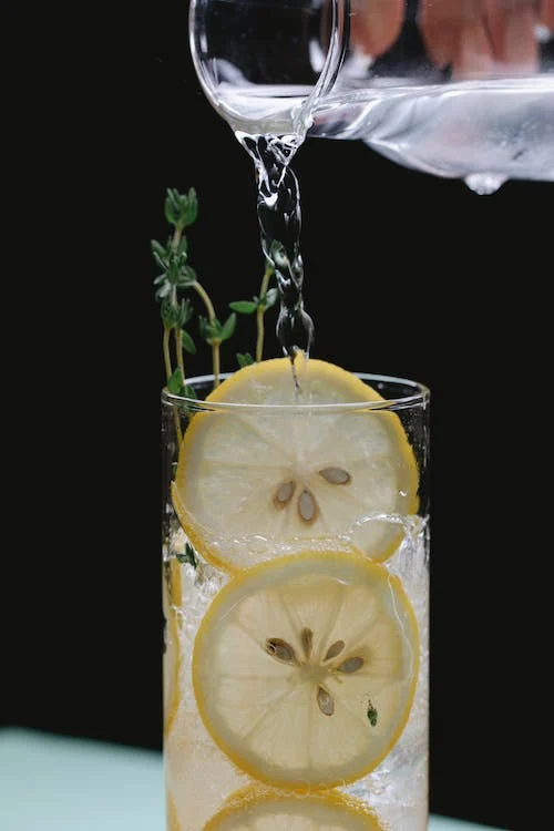 person pouring liquid from a glass jug into a glass with lemon