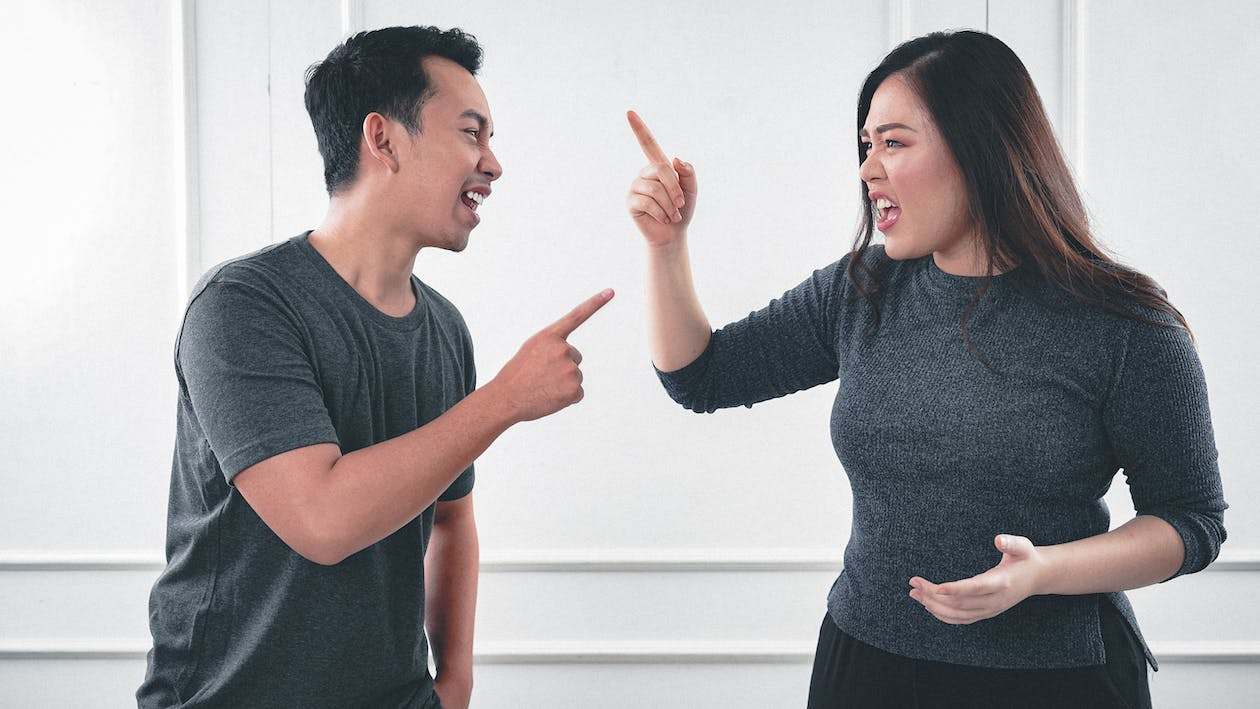 A man and woman wearing gray shirts, both pointing fingers