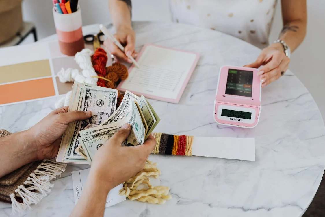 A person handing a money to a woman with pink calculator and notebook