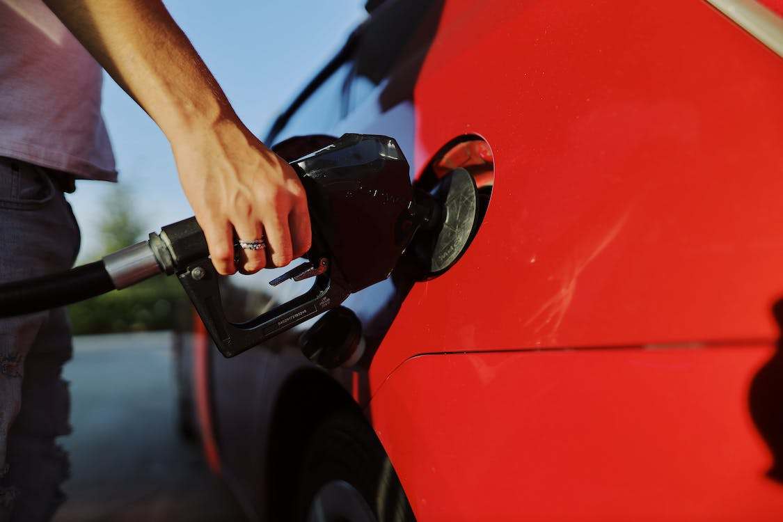 A person holding a fuel nozzle on a red car