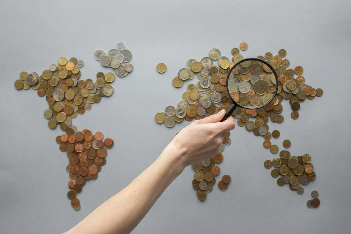 A person holding a magnifying glass above coins shaped like a map