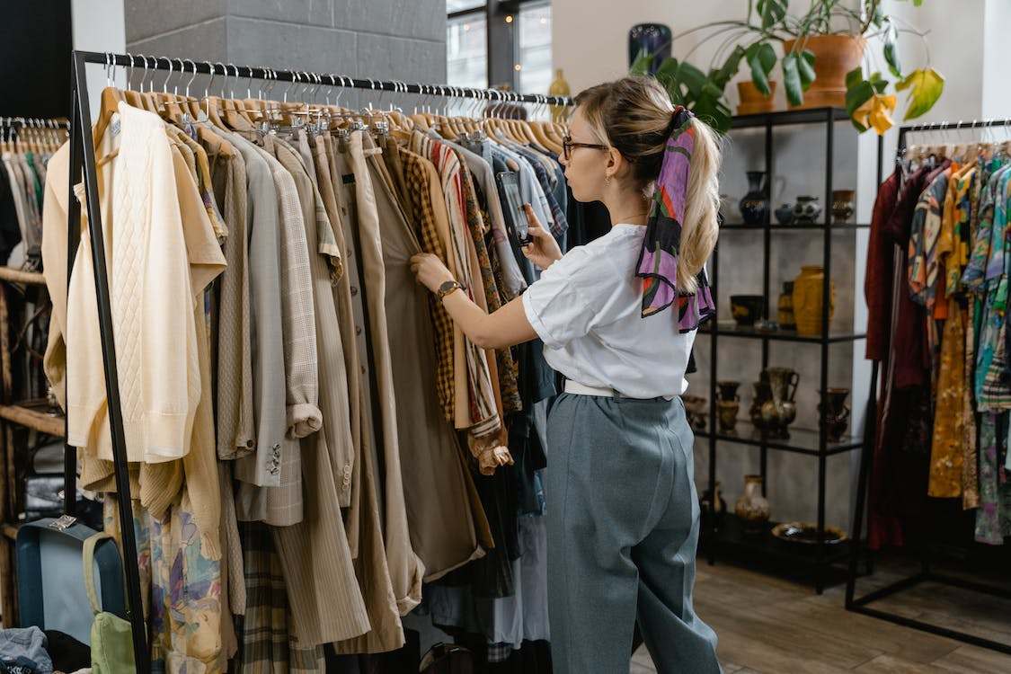 A woman in white shirt and gray trousers choosing clothes from the rack