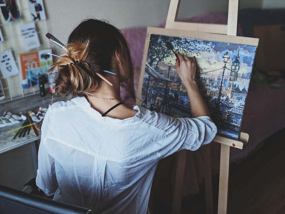 A woman in white shirt painting a canvas