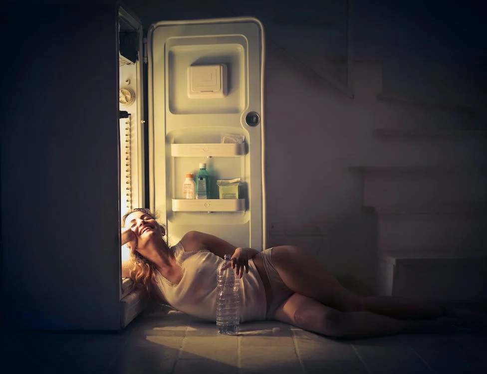 A woman lying on the floor with an open refrigerator