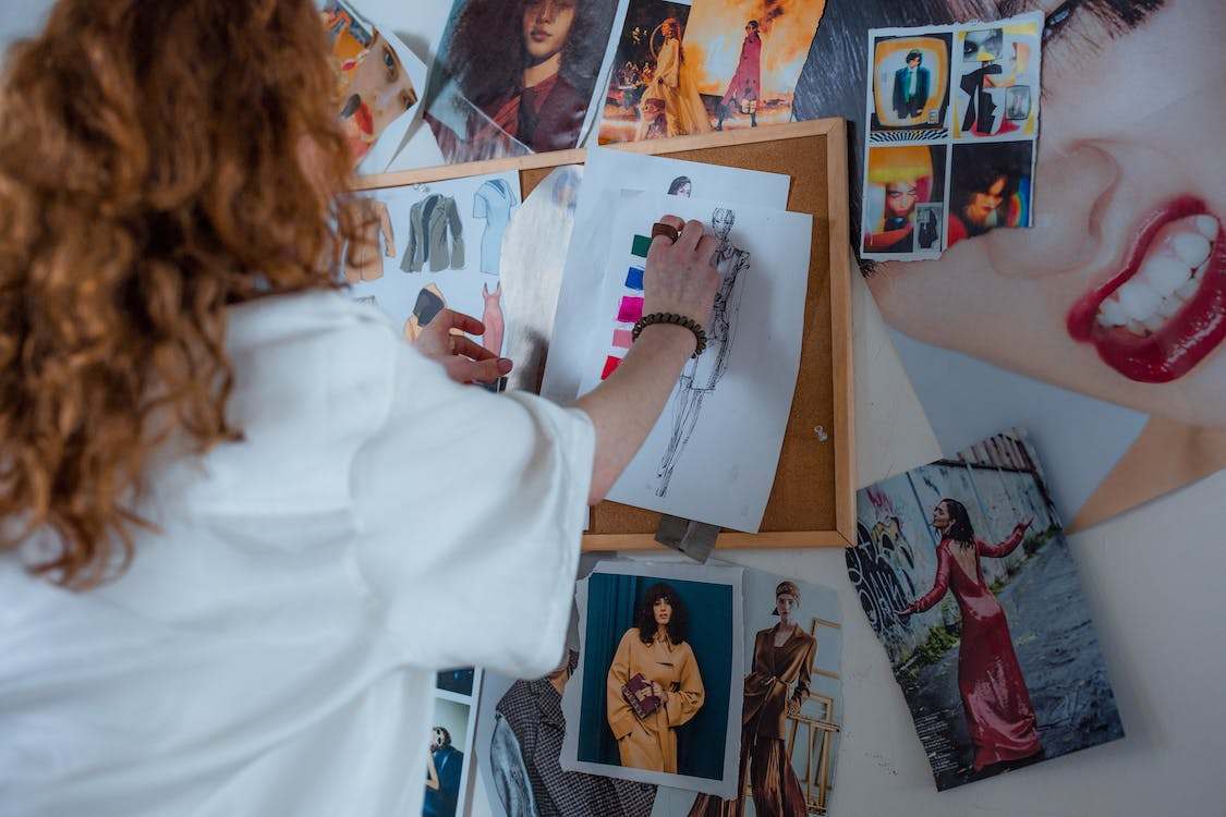 A woman with curly hair and wearing white shirt putting sketches on a corkboard