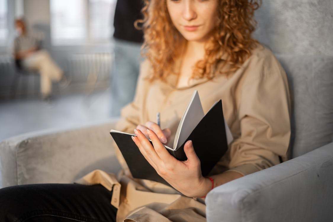 A woman with curly hair writing on a black notebook