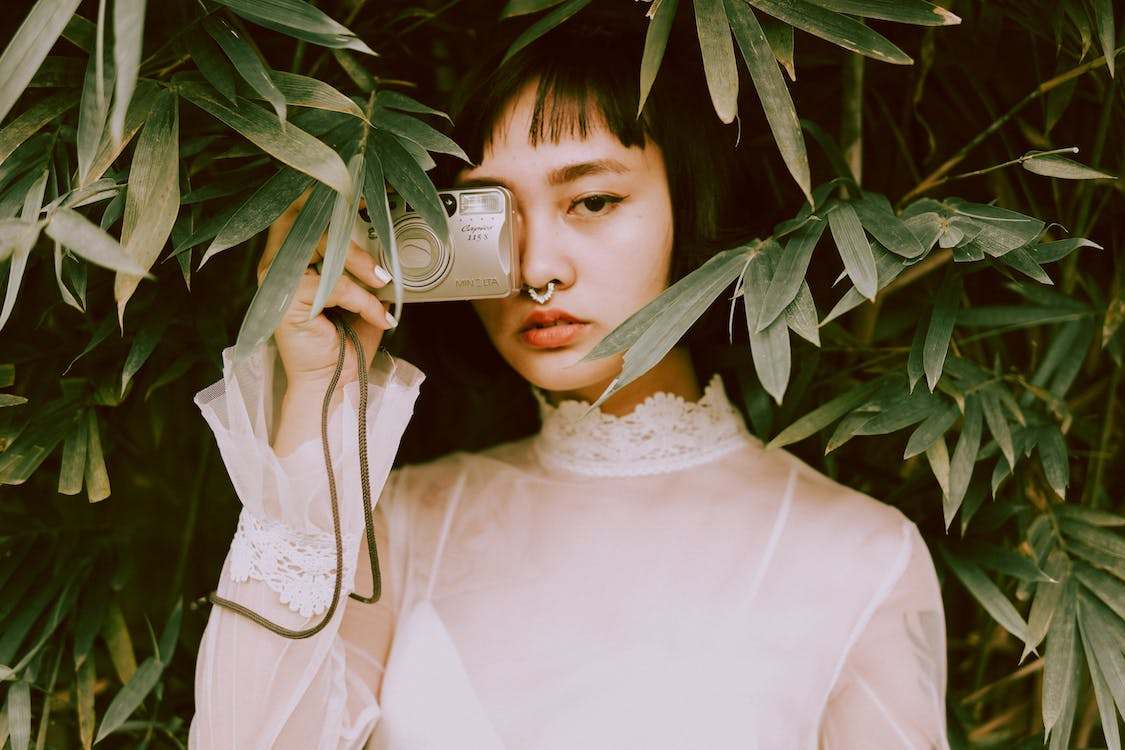An Asian women with short hair and nose piercing, holding a camera