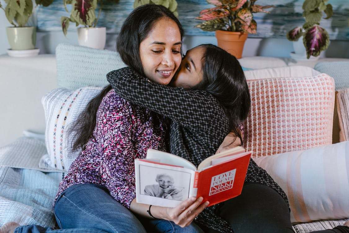 Daughter hugging mother while reading a book