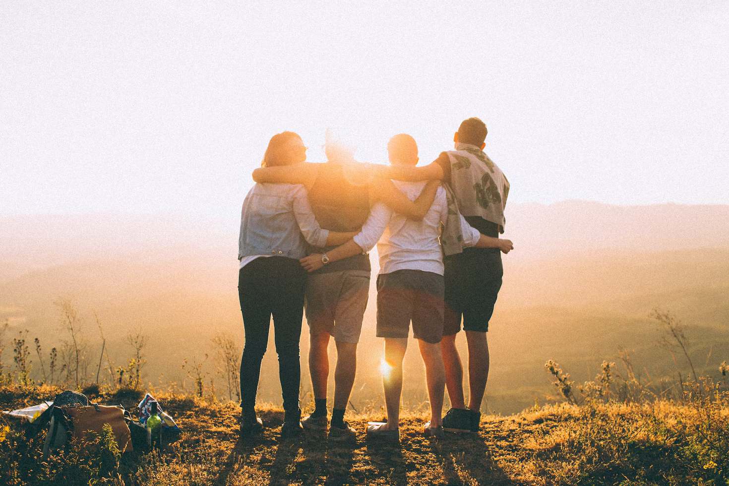 Four persons with hands wrap around shoulders while looking at sunset
