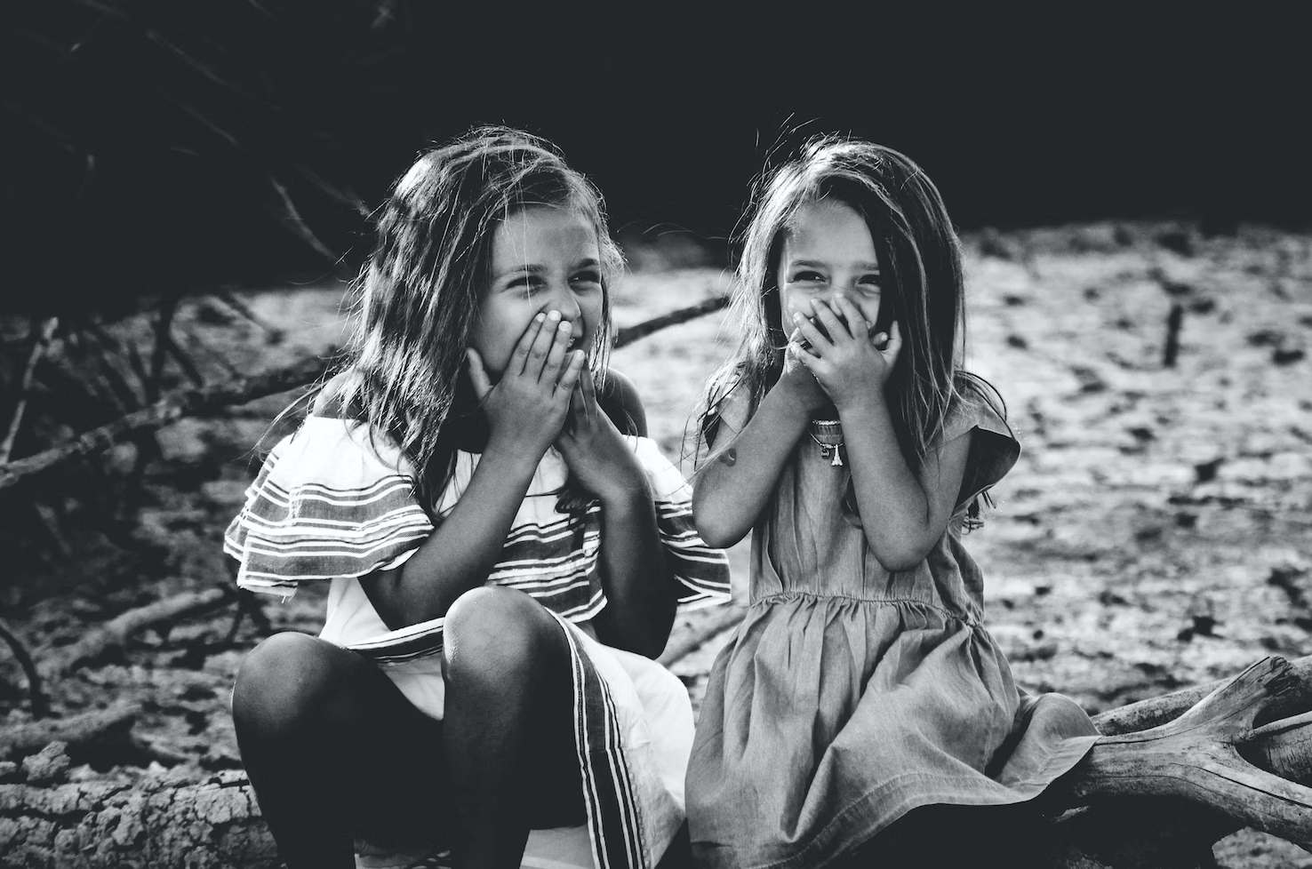 Grayscale photography of two girls laughing covering their mouths