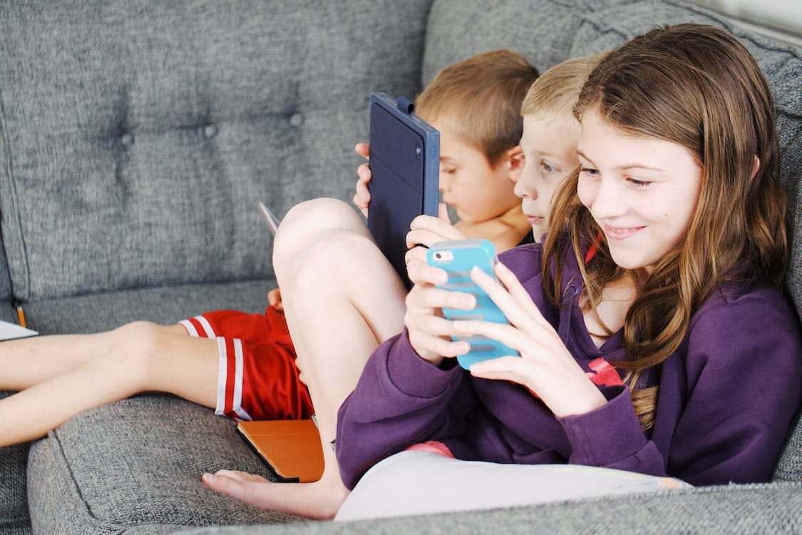 Photo of kids using smartphones sitting on gray sofa