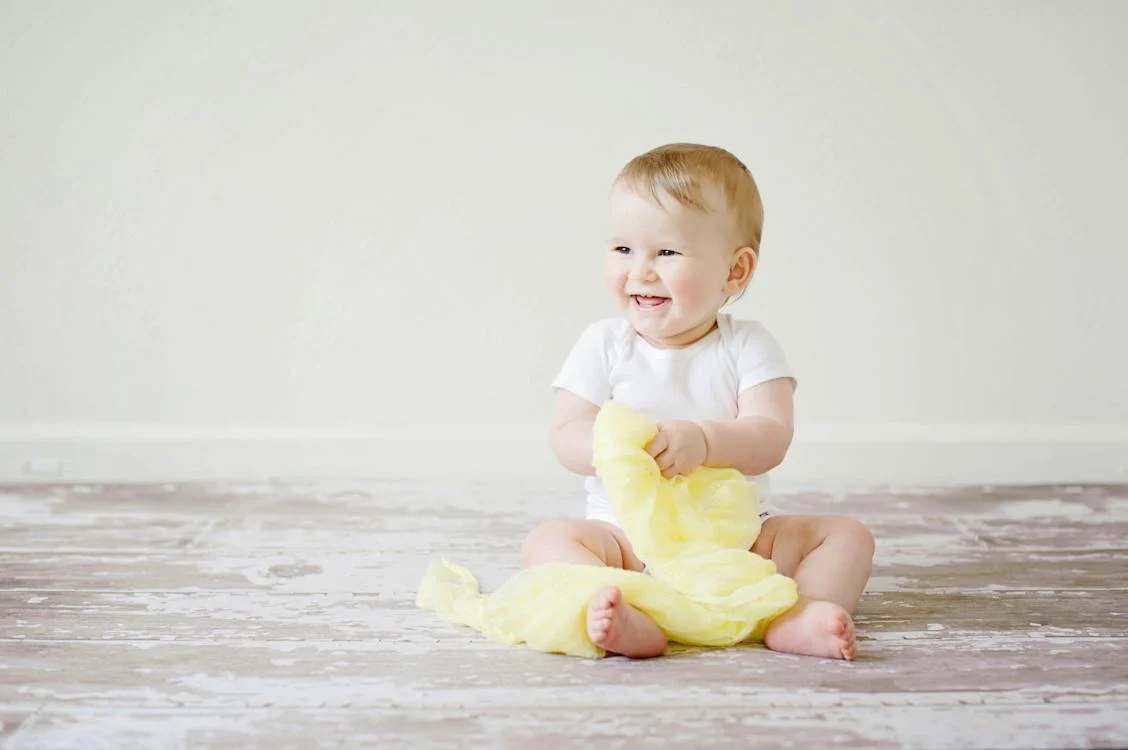 Toddler Sitting while smiling and holding a yellow cloth