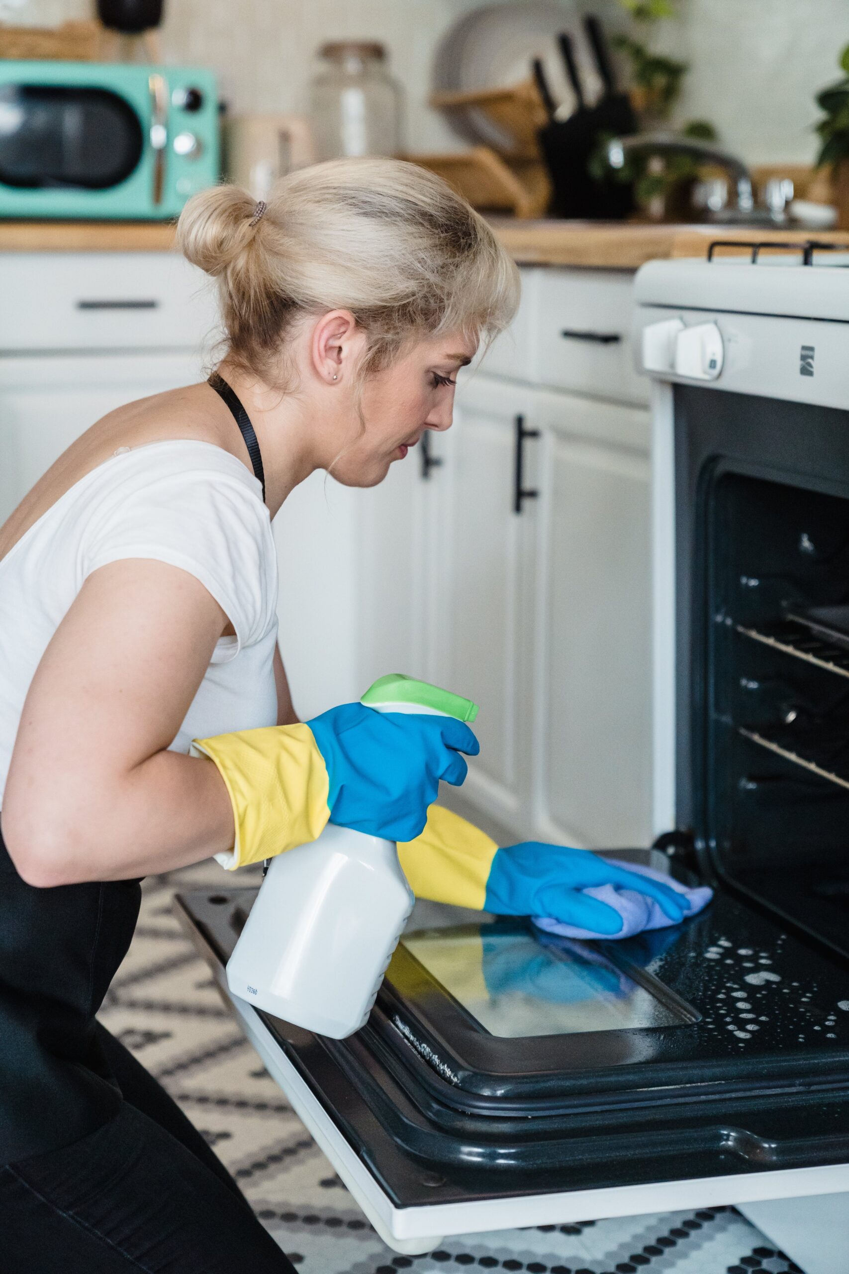 woman in white shirt holding white and green plastic spray bottle cleaning the oven