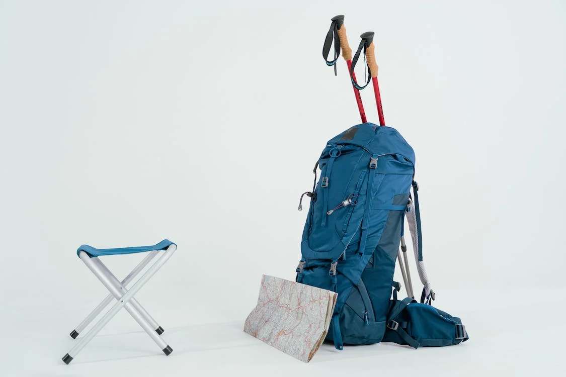 A blue hiking backpack with other traveling equipment and accessories on the side