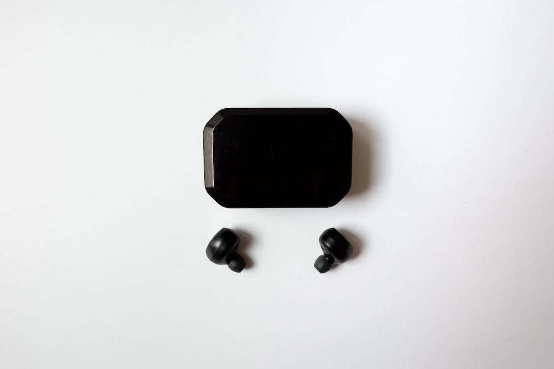 A pair of black wireless earbuds on a white surface