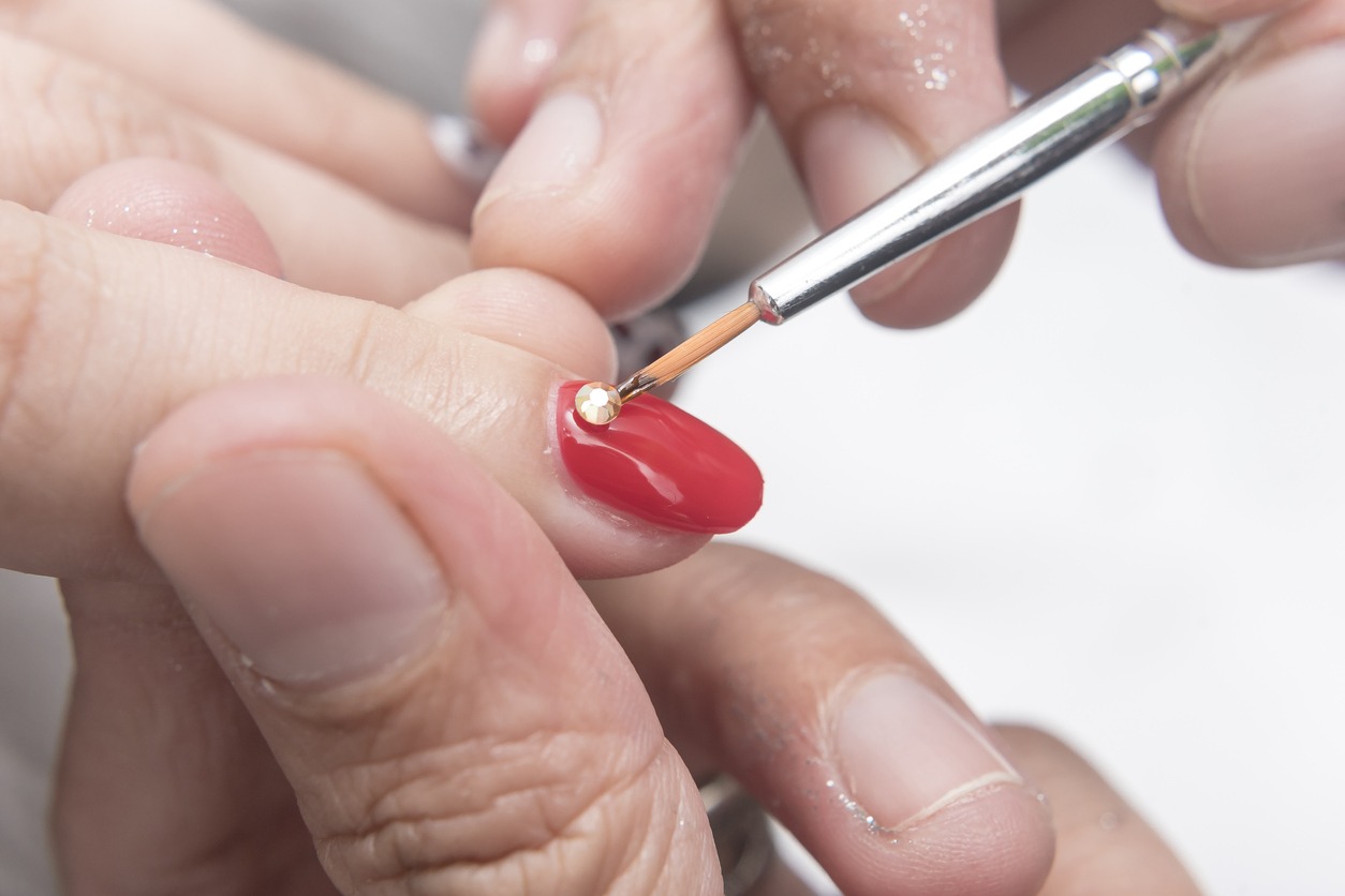 Placing small gold gemstones on the surface of a polished red nail
