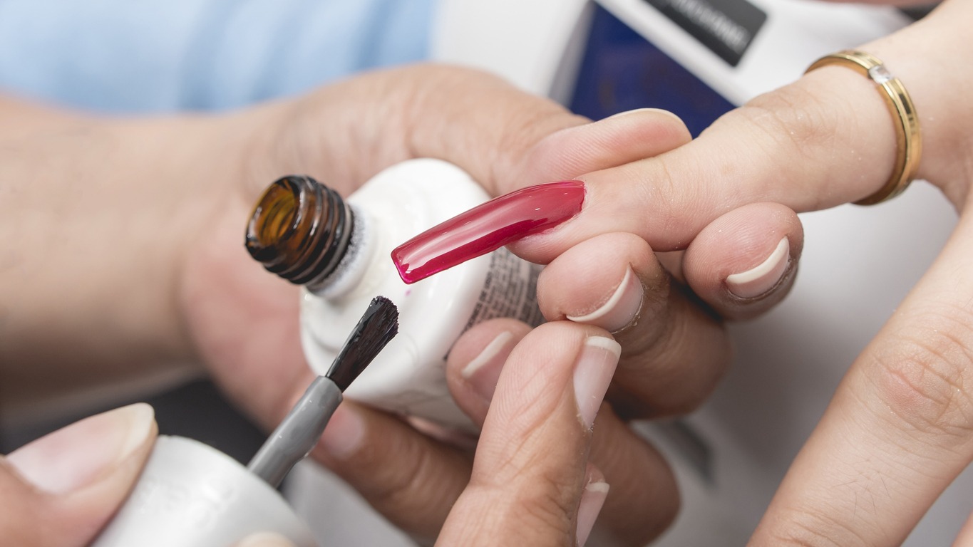 A manicurist applies a deep red gel coat nail polish