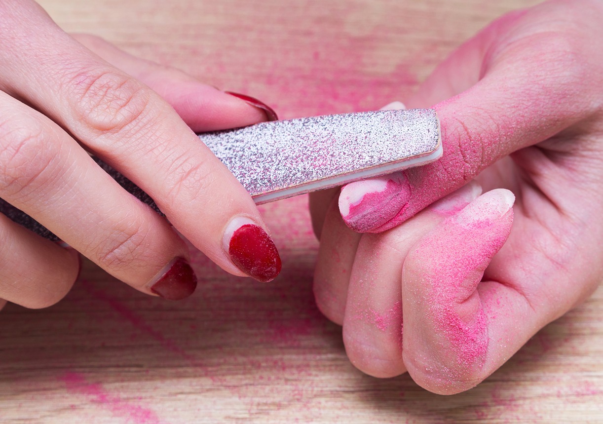 Woman does manicure at home and using a nail file removes old gel polish from her nails