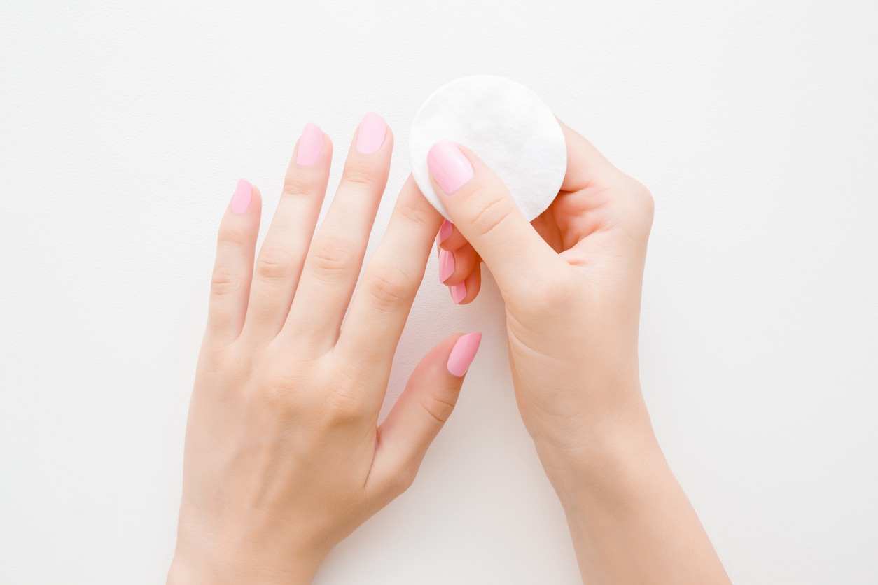 Woman's hand removing pink nail polish with white cotton pad 